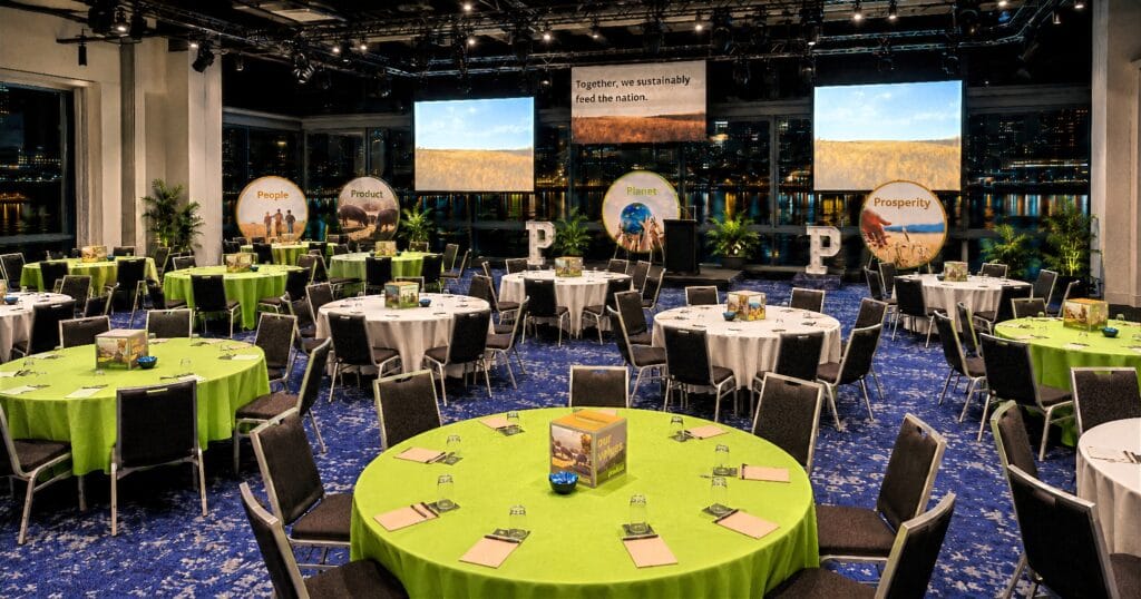 Rebrand launch event room with branded stage screens, green table settings and audience seating