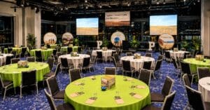 Rebrand launch event room with branded stage screens, green table settings and audience seating for an amazing brand experience
